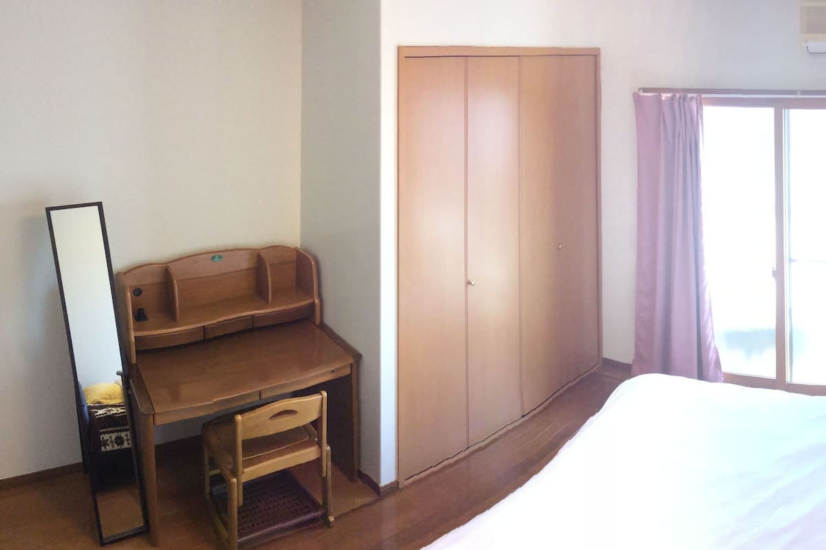 A bedroom with a bed, a desk, a wardrobe, and a window with curtains.