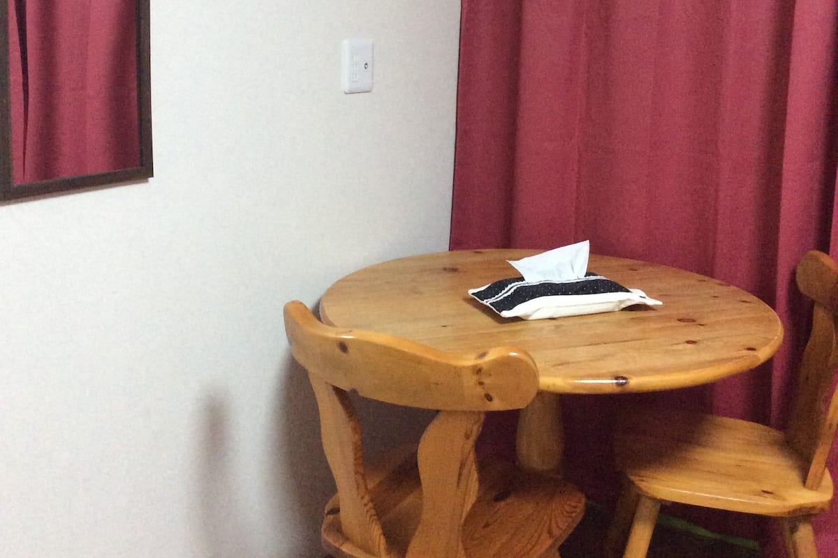 A small round wooden table with two chairs, a mirror on the wall, and red curtains.