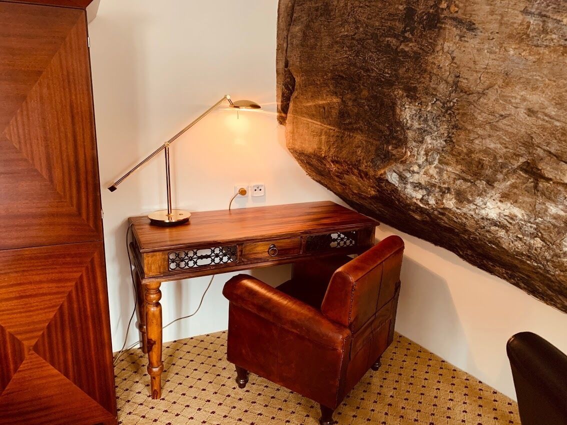 A wooden desk with a lamp, a leather chair, and a large rock wall.