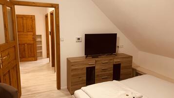 A bedroom with a wooden dresser, a television on top, a bed with white bedding, and a wooden wardrobe.