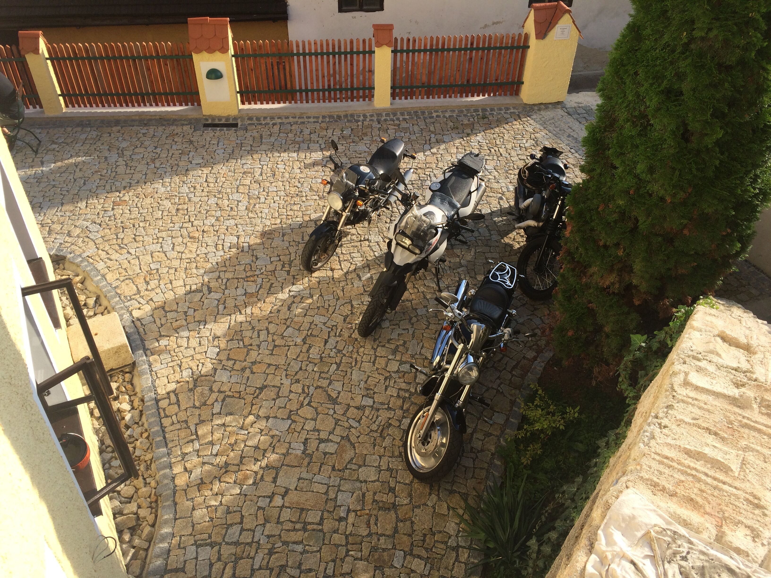A courtyard with a cobblestone floor, several parked motorcycles, and a green tree.