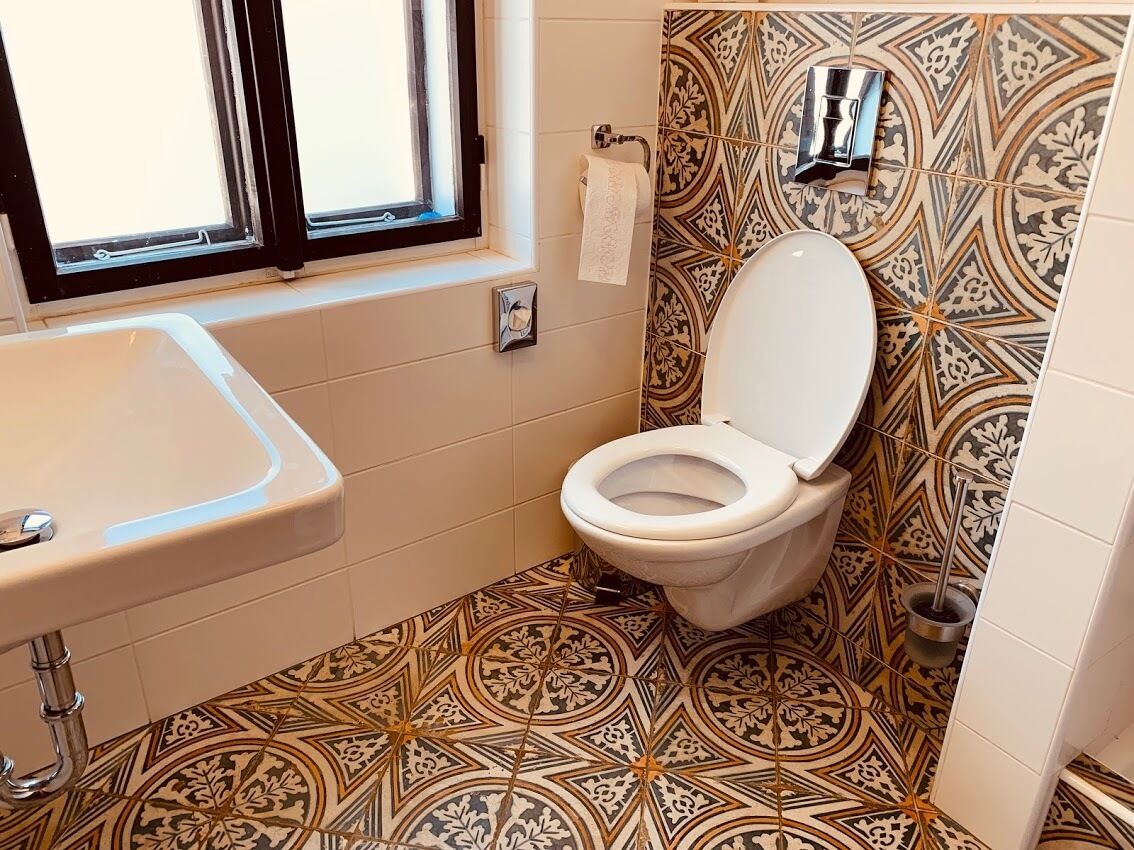 A bathroom with a patterned tile floor, a toilet, a sink, and a window.