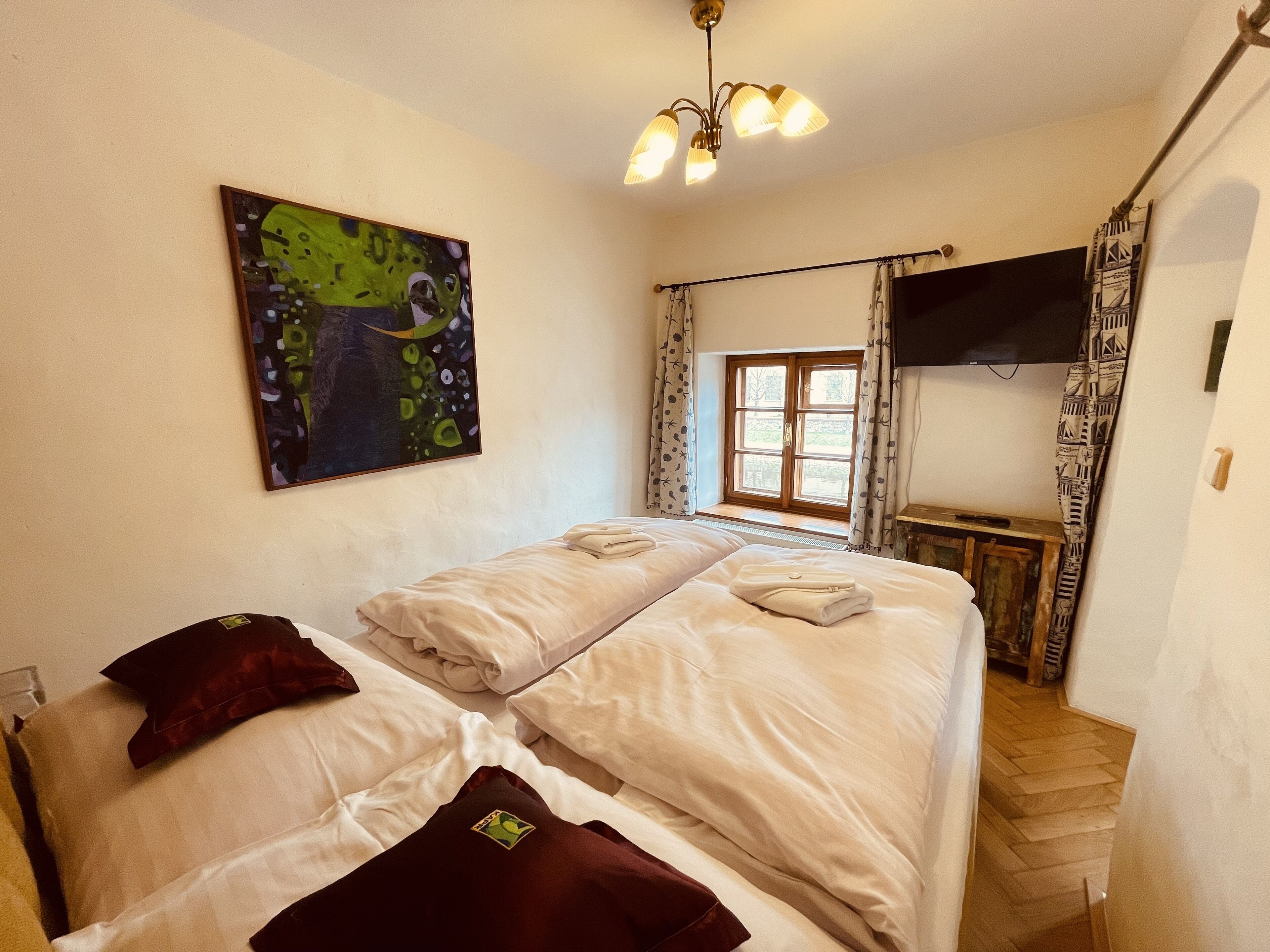 A hotel room with two beds, a painting on the wall, a window with curtains, a television, and a staircase.