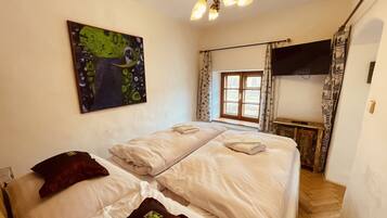 A hotel room with two beds, a painting on the wall, a window with curtains, a television, and a staircase.