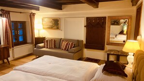 A bedroom with a large bed, a sofa, a bedside table, a lamp, a window with curtains, a mirror, and a painting on the wall. - Penzion Kapr (Cesky Krumlov)
