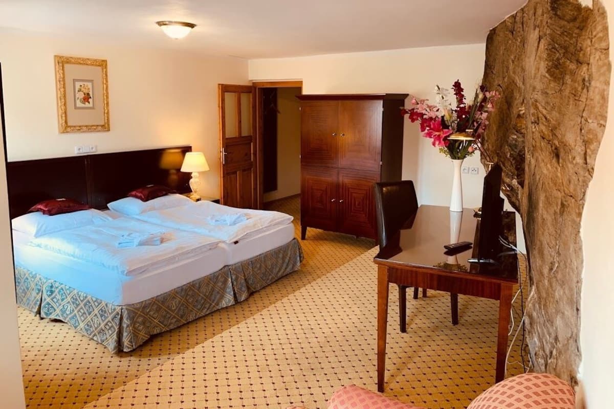 A hotel room with a bed, a desk, a chair, a wardrobe, and a large rock-like feature.