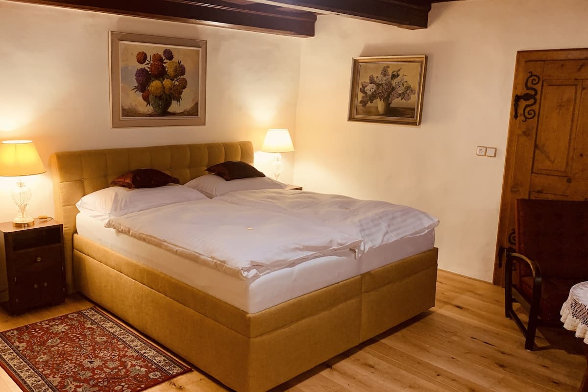 A bedroom with a large bed, two bedside lamps, a wooden headboard, a red patterned rug, and two framed floral paintings on the walls.