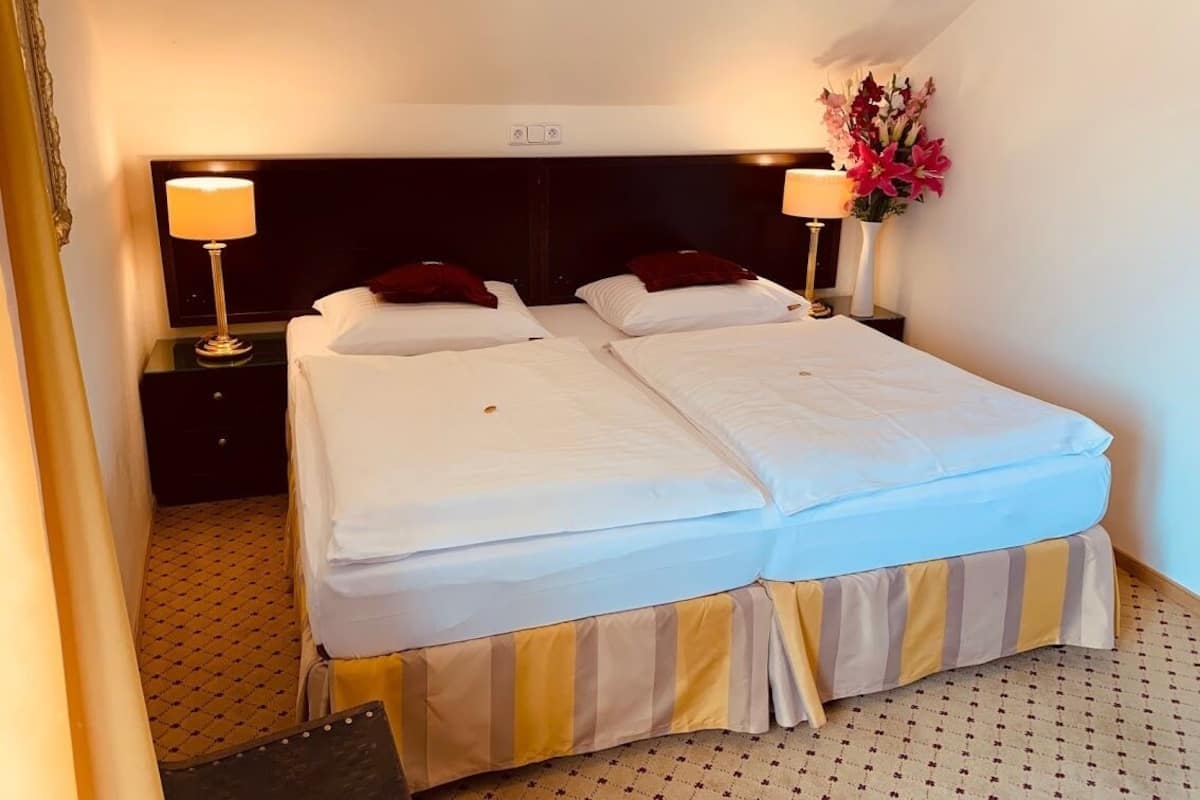A double bed with white linens, two bedside tables with lamps, a dark headboard, and a vase with flowers.