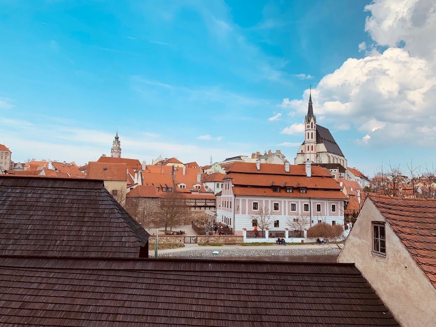 Vista de un pueblo con edificios históricos, una iglesia destacada con un campanario alto y un muro de piedra en primer plano.