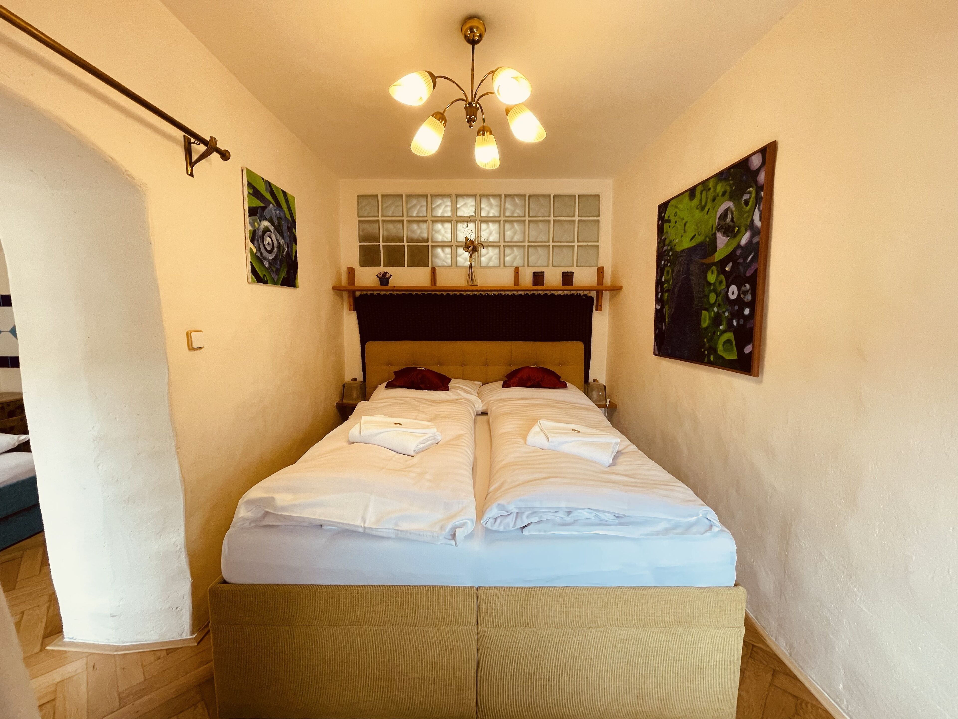 A double bed with white linens, a wooden headboard, and a ceiling light fixture.