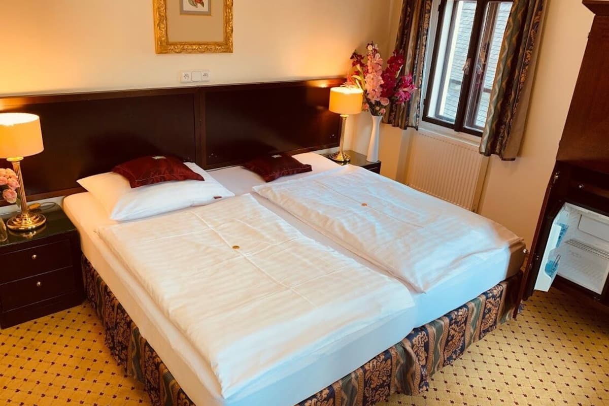 A hotel room with a large bed, two bedside tables, a lamp, a picture frame, and a window with curtains.