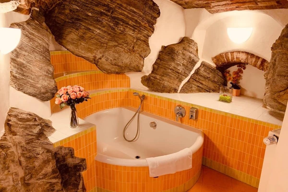 A bathroom with a large bathtub, tiled walls, and a stone archway.
