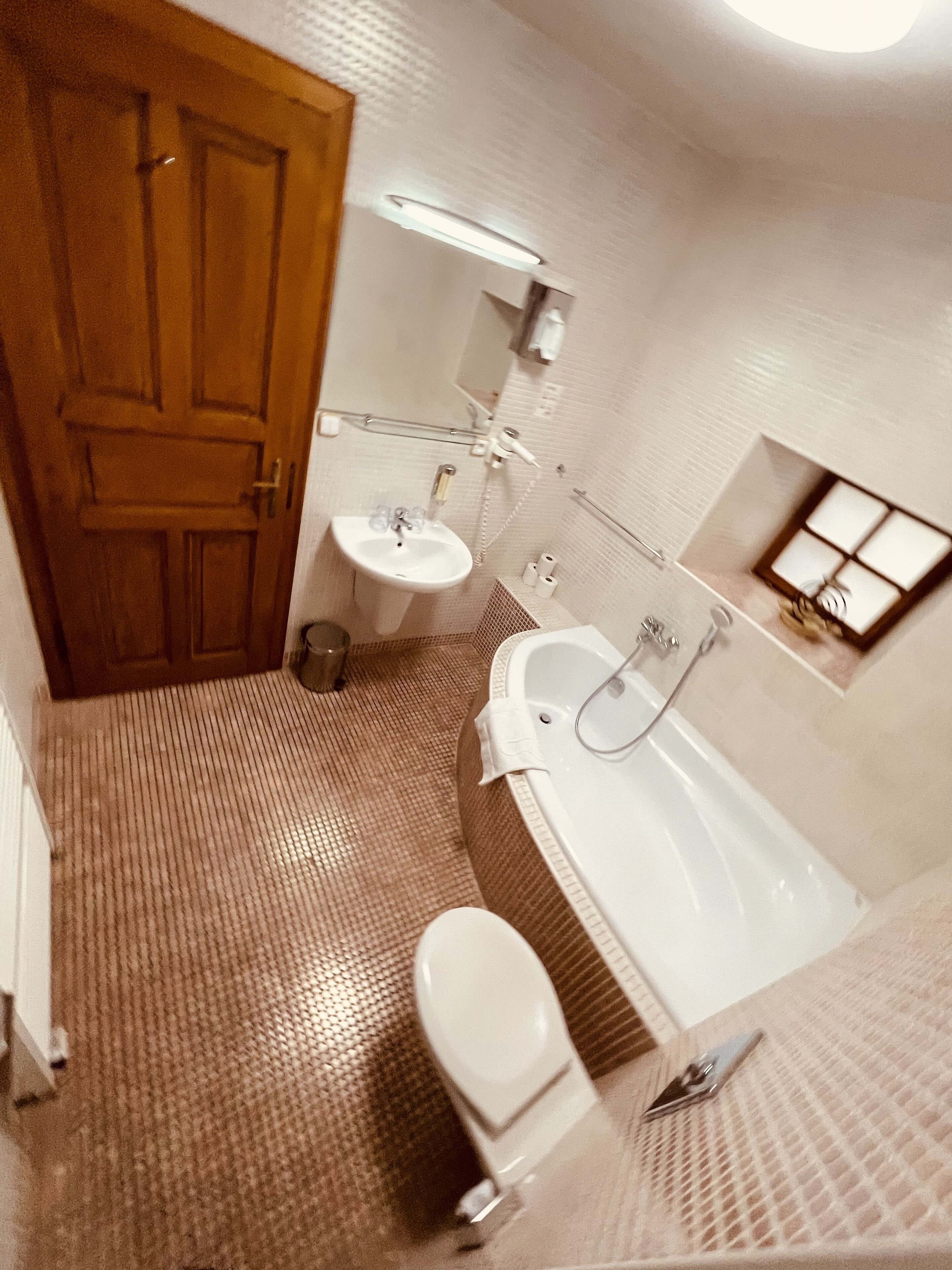 A bathroom with a wooden door, a sink, a bathtub, and a small window.