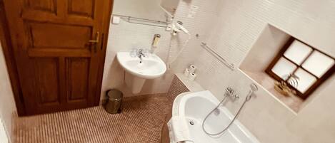 A bathroom with a wooden door, a sink, a bathtub, and a small window.