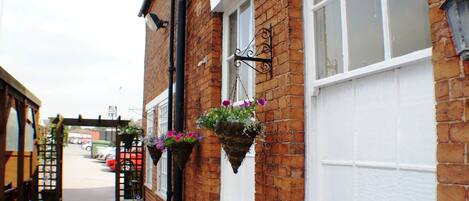 A narrow brick alley with hanging flower baskets and a white door.