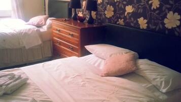 A hotel room with two beds, a wooden dresser, and a floral wallpaper.