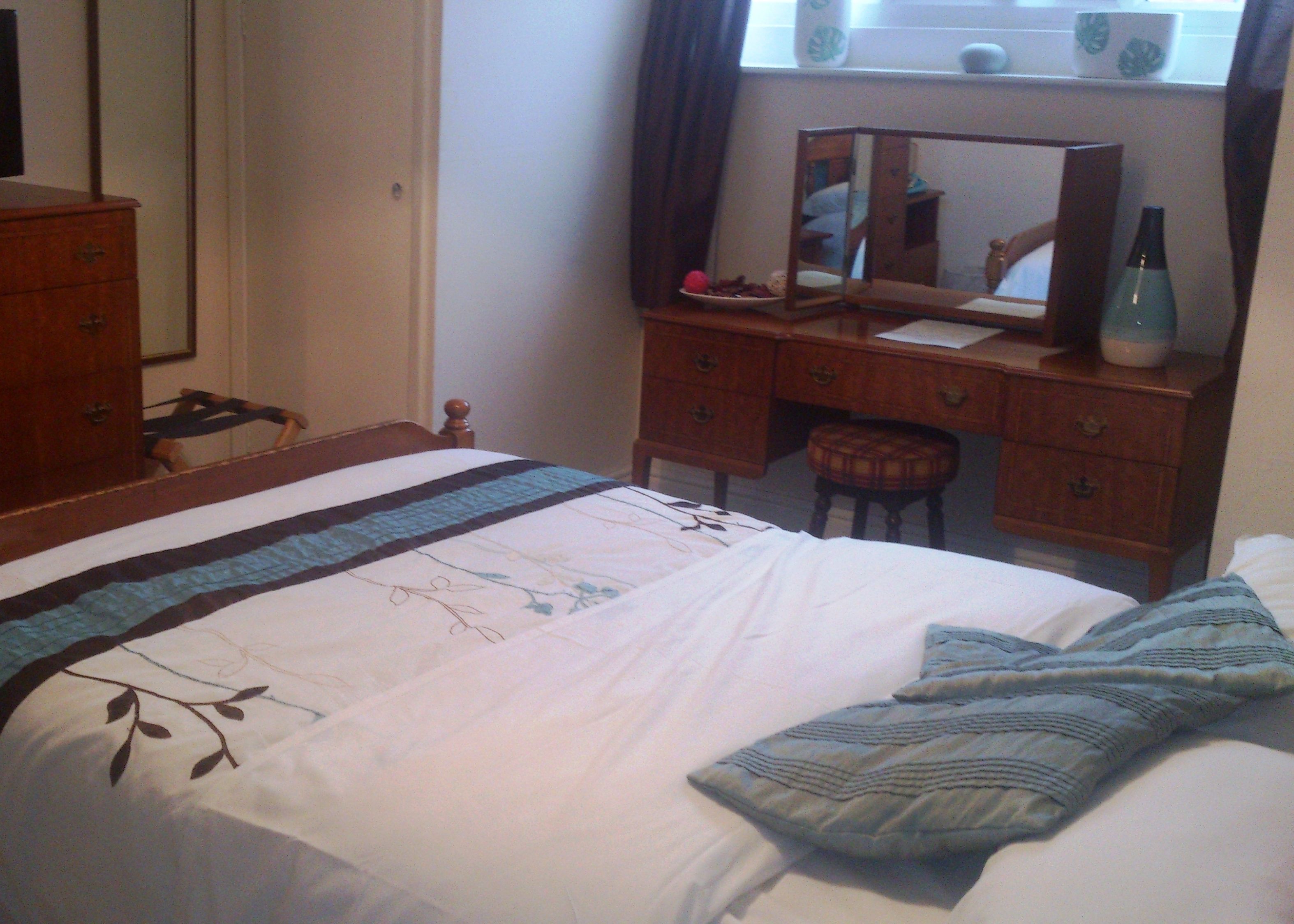 A bedroom with a bed, a wooden dresser, a mirror, and a window with curtains.