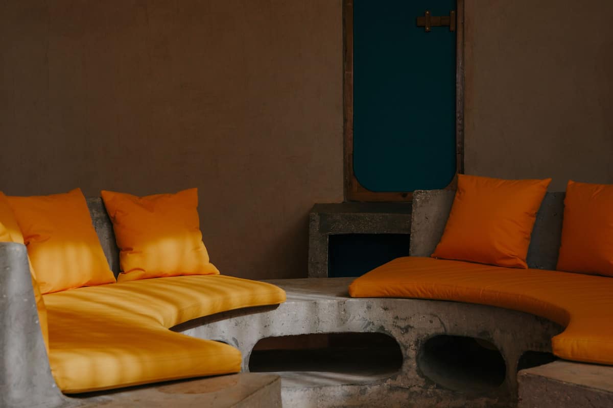 Ein Zimmer mit einer gebogenen Steinbank und orangefarbenen Kissen.