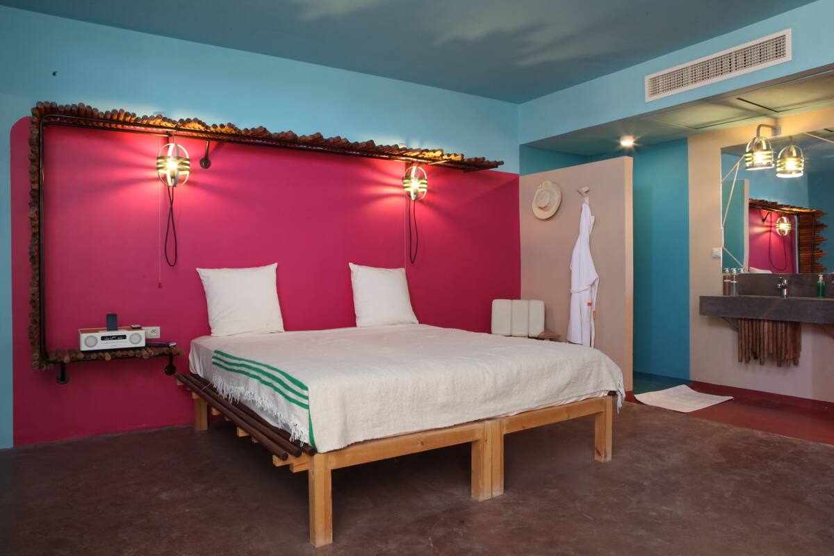 Ein Schlafzimmer mit einem hölzernen Bett, pinken und blauen Wänden, einem Schminktisch mit Spiegel und Wandleuchten.