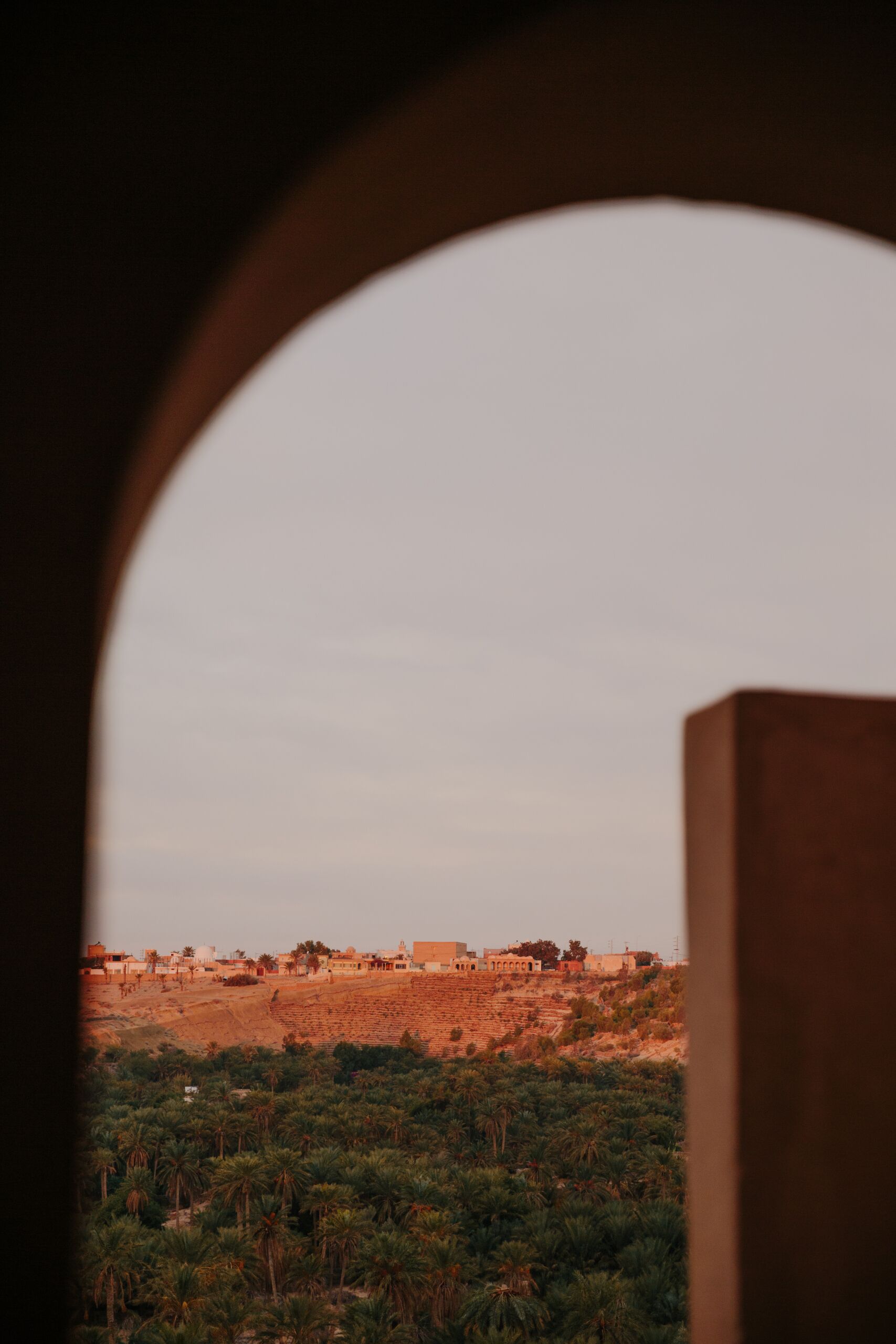 Vista a través de un arco de un paisaje con edificios y vegetación.