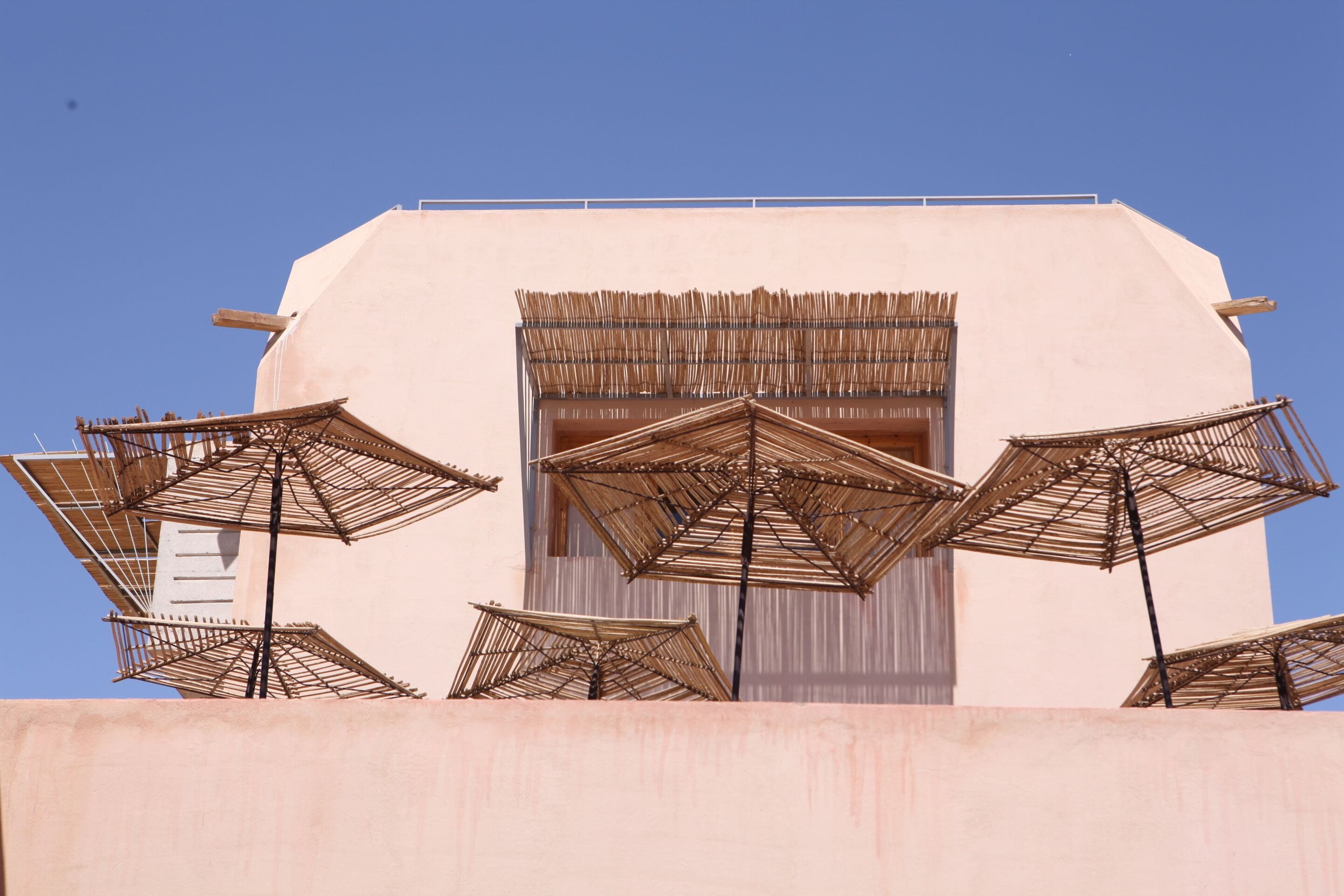 Un bâtiment à la façade plate, surmonté de plusieurs parasols en chaume.