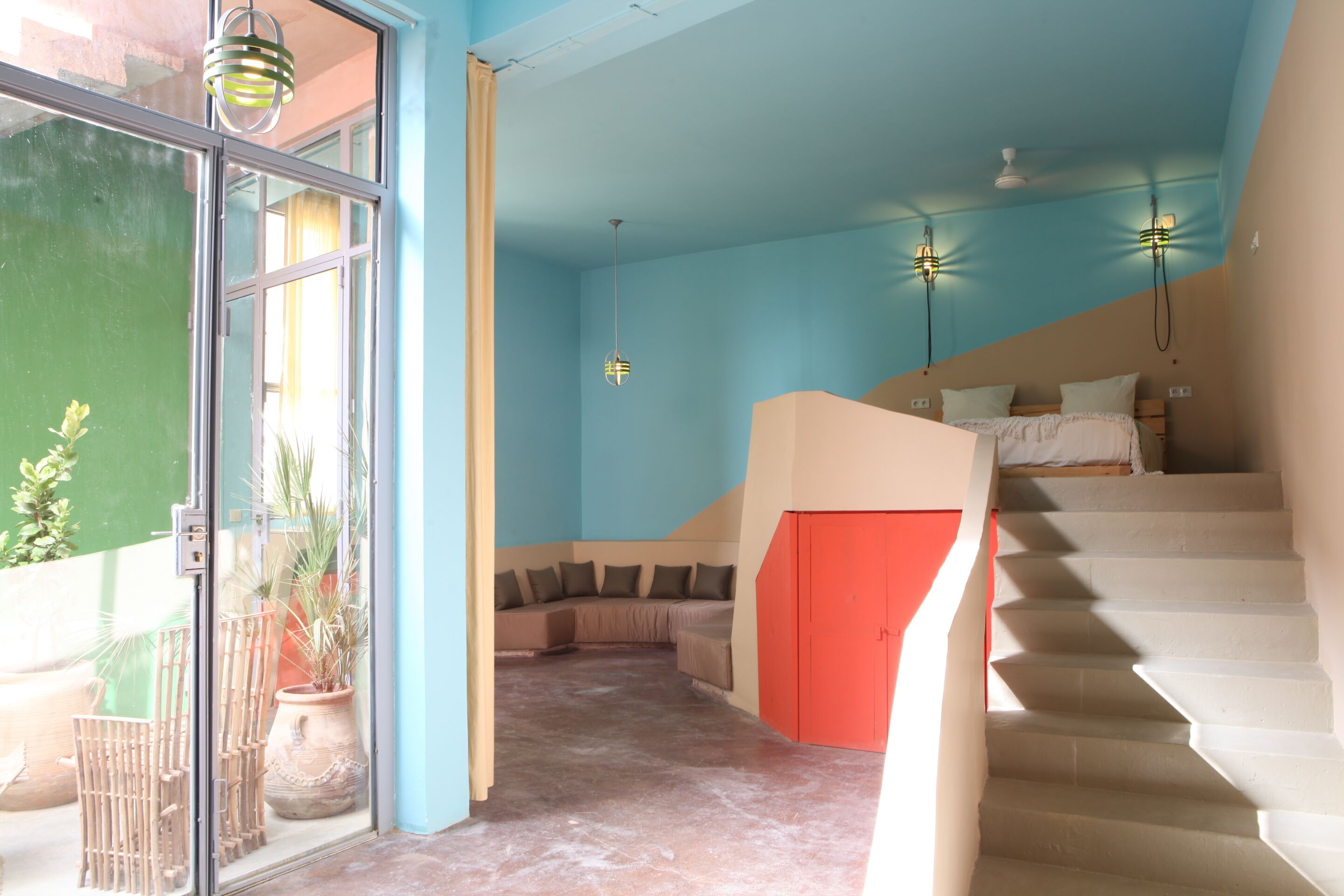 A room with a bed, a staircase, and a door leading to an outdoor area with plants.