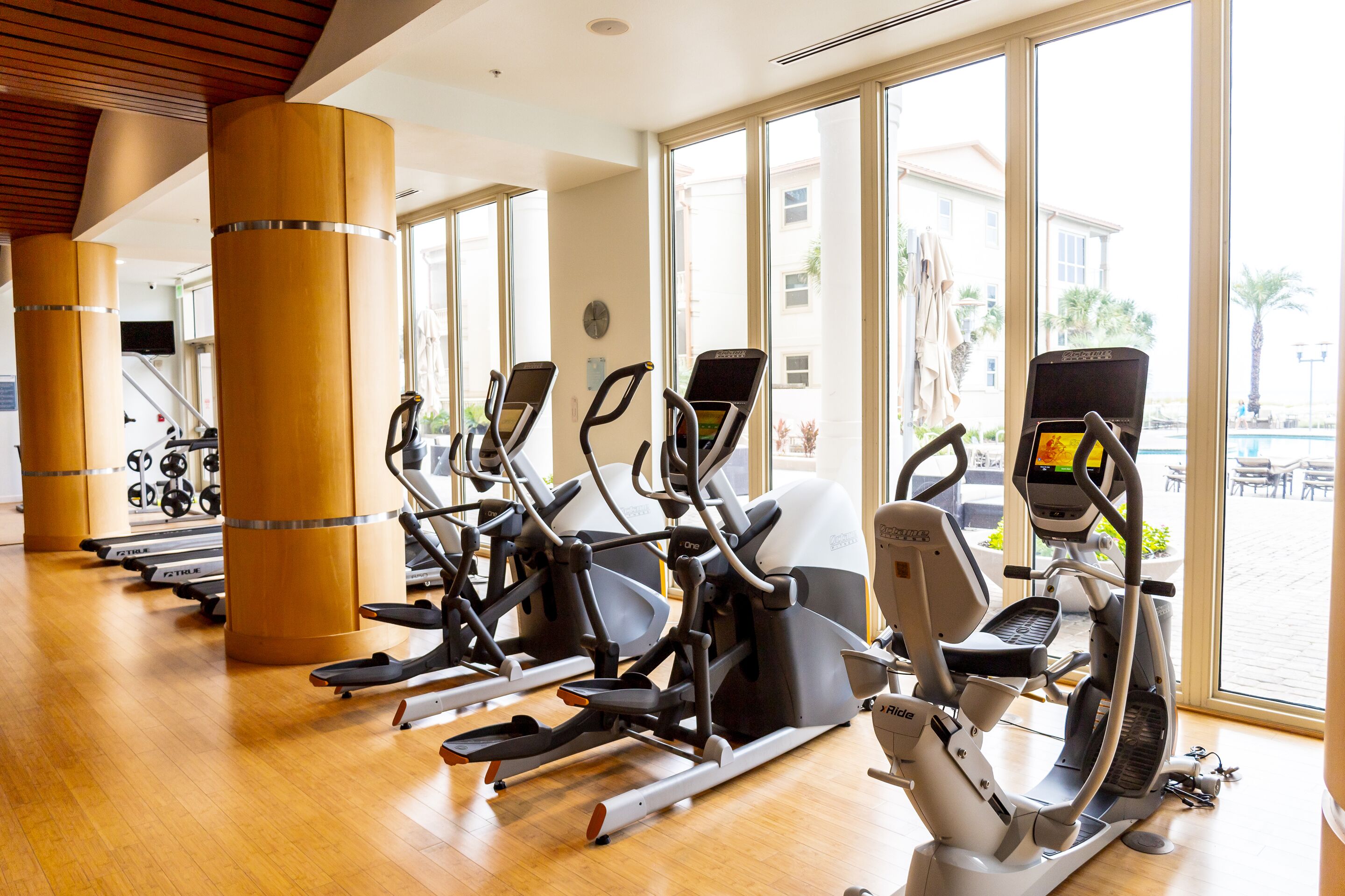 Een sportschool met cardioapparatuur en grote ramen.