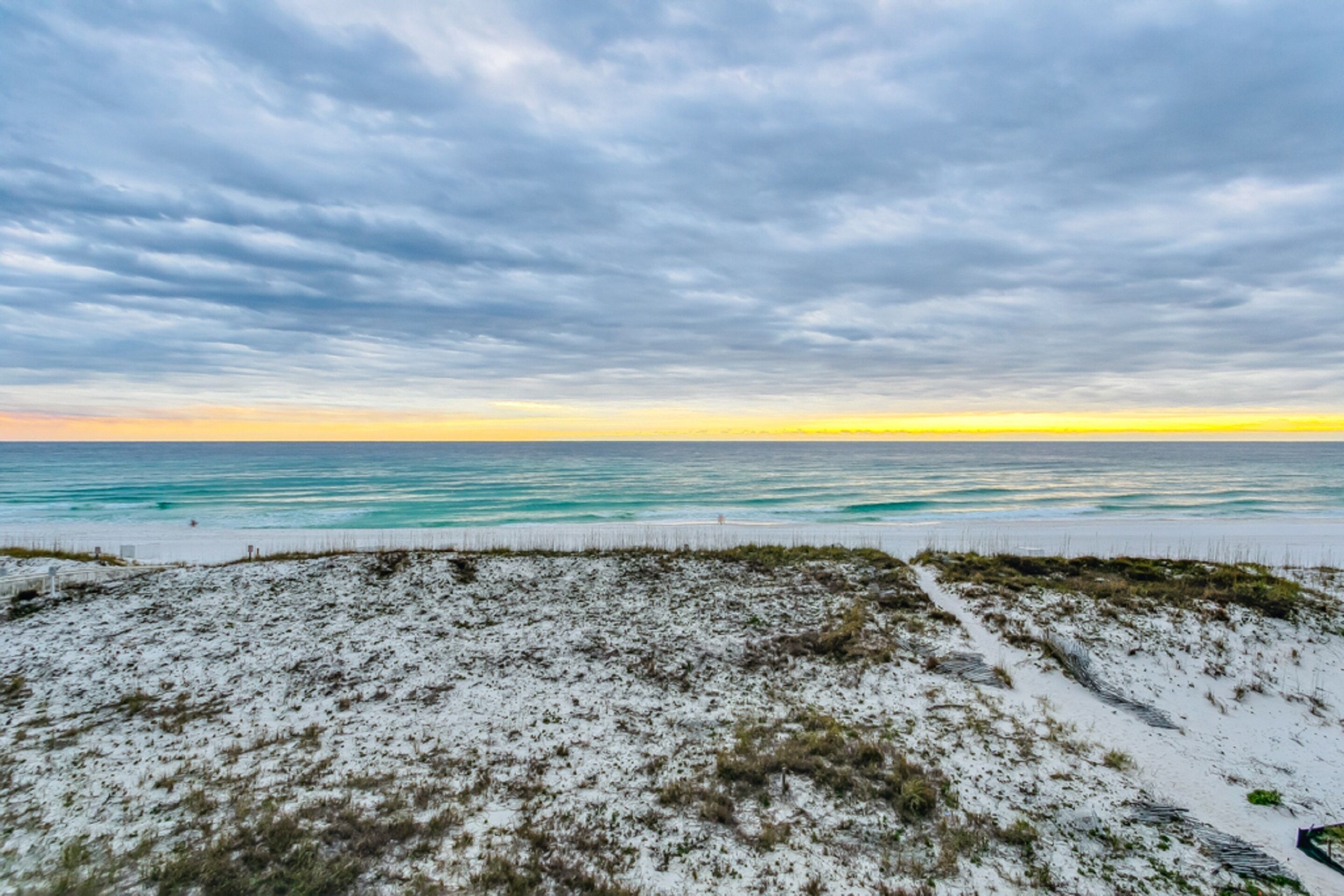 A beach with a sandy foreground and a view of the ocean under a cloudy sky.