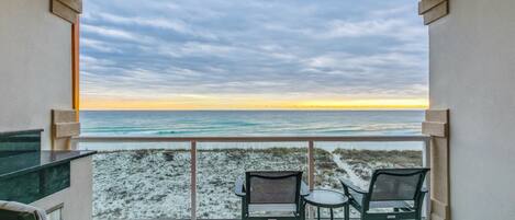 A balcony with a view of the beach and ocean. There are two chairs and a small table.
