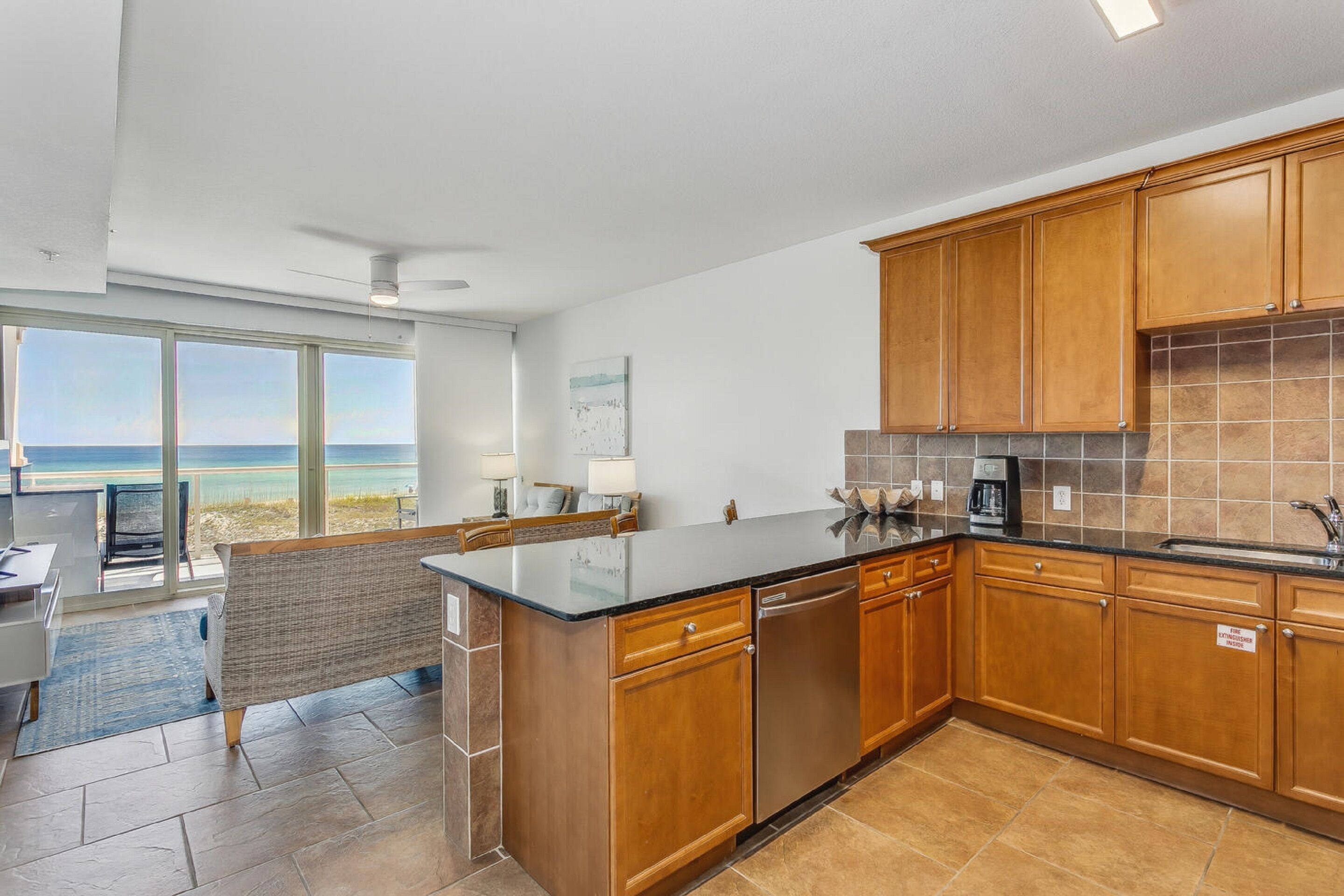 A modern kitchen with wooden cabinets, a black countertop, and a view of the ocean through large windows.