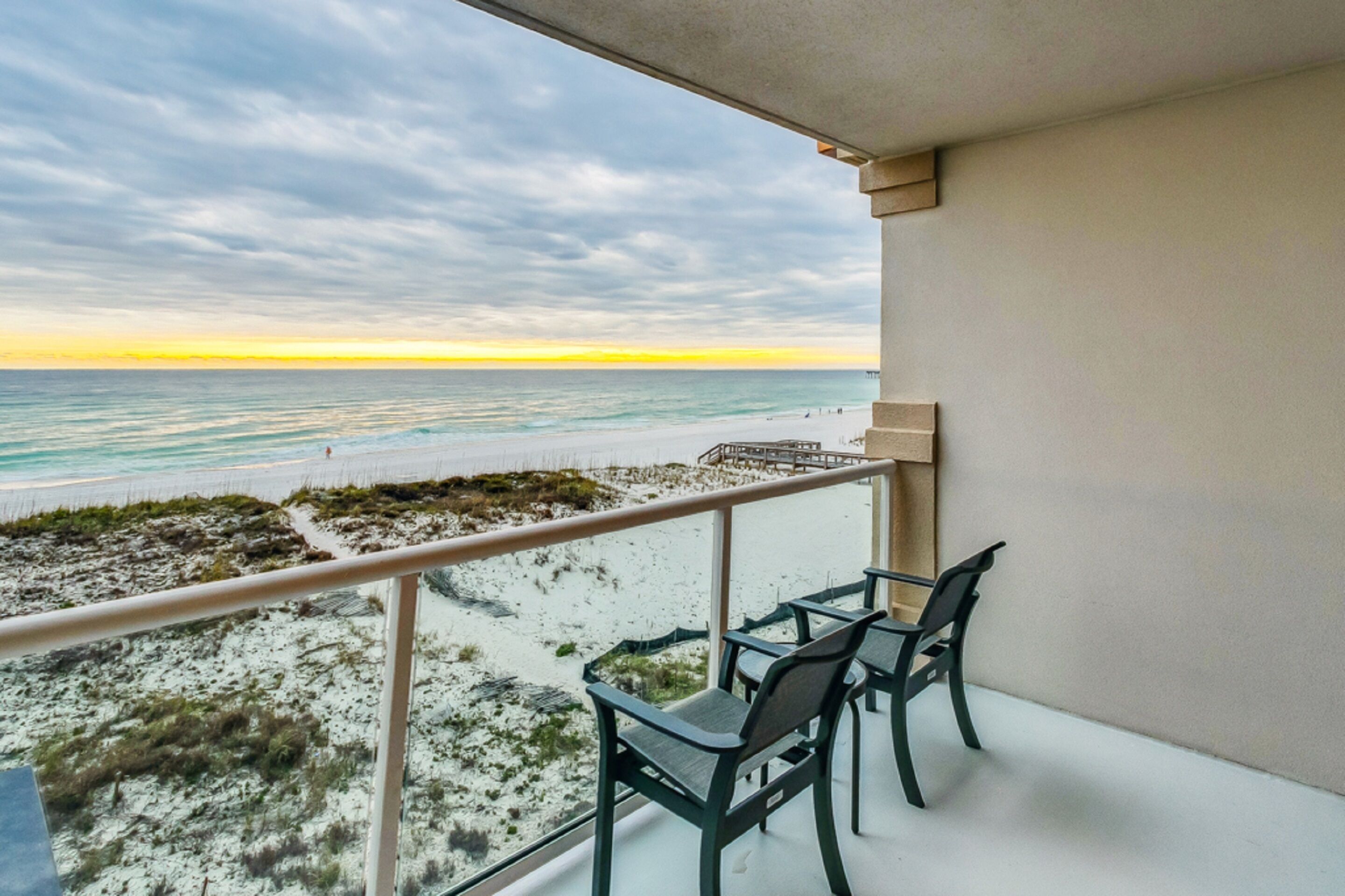 Un balcón con vista a la playa y al océano al atardecer.