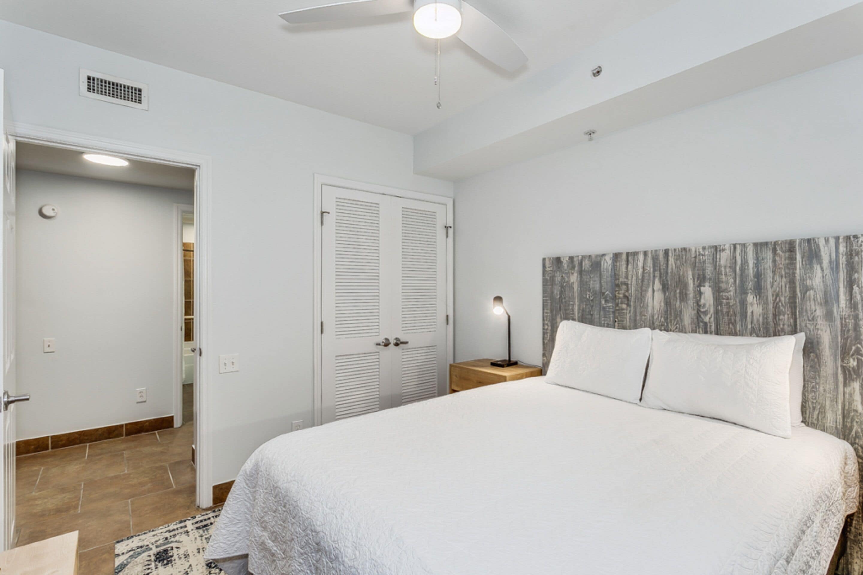 A bedroom with a bed, a nightstand, a ceiling fan, and a door.
