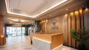 A hotel reception area with a wooden reception desk, a sign reading "TEATRO BOUTIQUE HOTEL," and a large potted plant to the right. - Teatro Boutique Hotel (Baku)