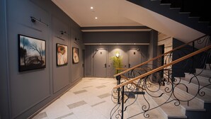 A modern interior with a staircase, framed artwork on the walls, and a hallway leading to a door. - Teatro Boutique Hotel (Baku)