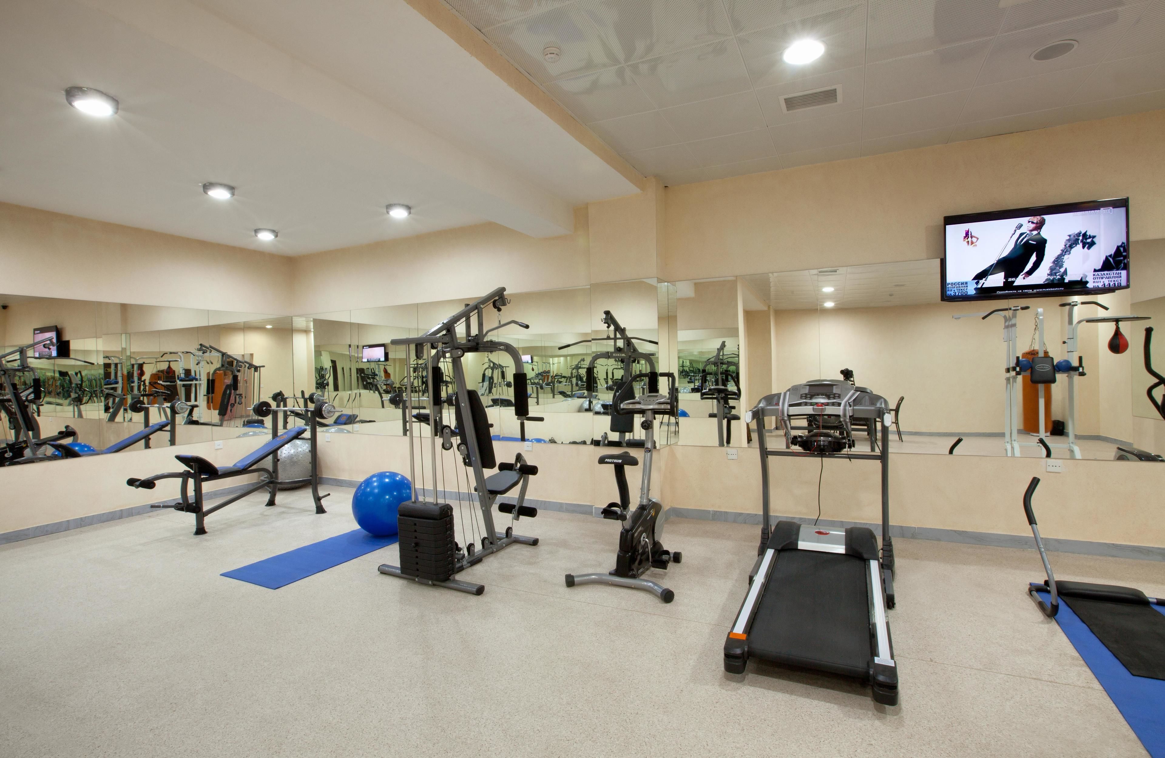 A gym with various exercise equipment, a treadmill, and a television screen.