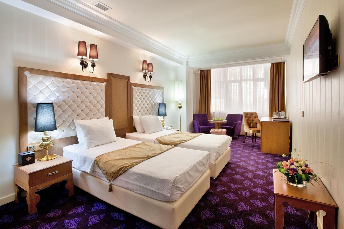 A hotel room with two beds, a desk, a chair, a TV, and a decorative vase.