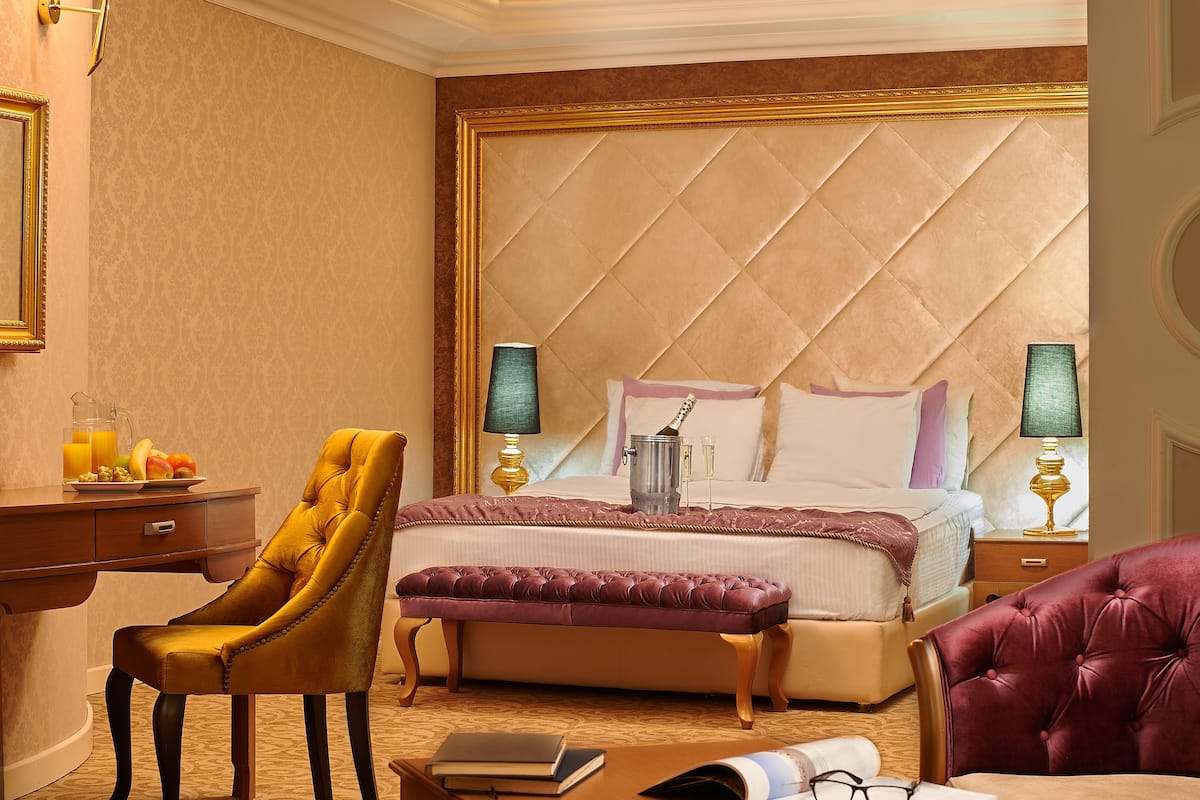 Een hotelkamer met een groot bed, een bureau met stoel, een bankje en een nachtkastje met lampen.