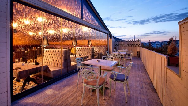 An outdoor dining area with tables and chairs, a glass wall with a patterned design, and a wooden deck. - Teatro Boutique Hotel (Baku)