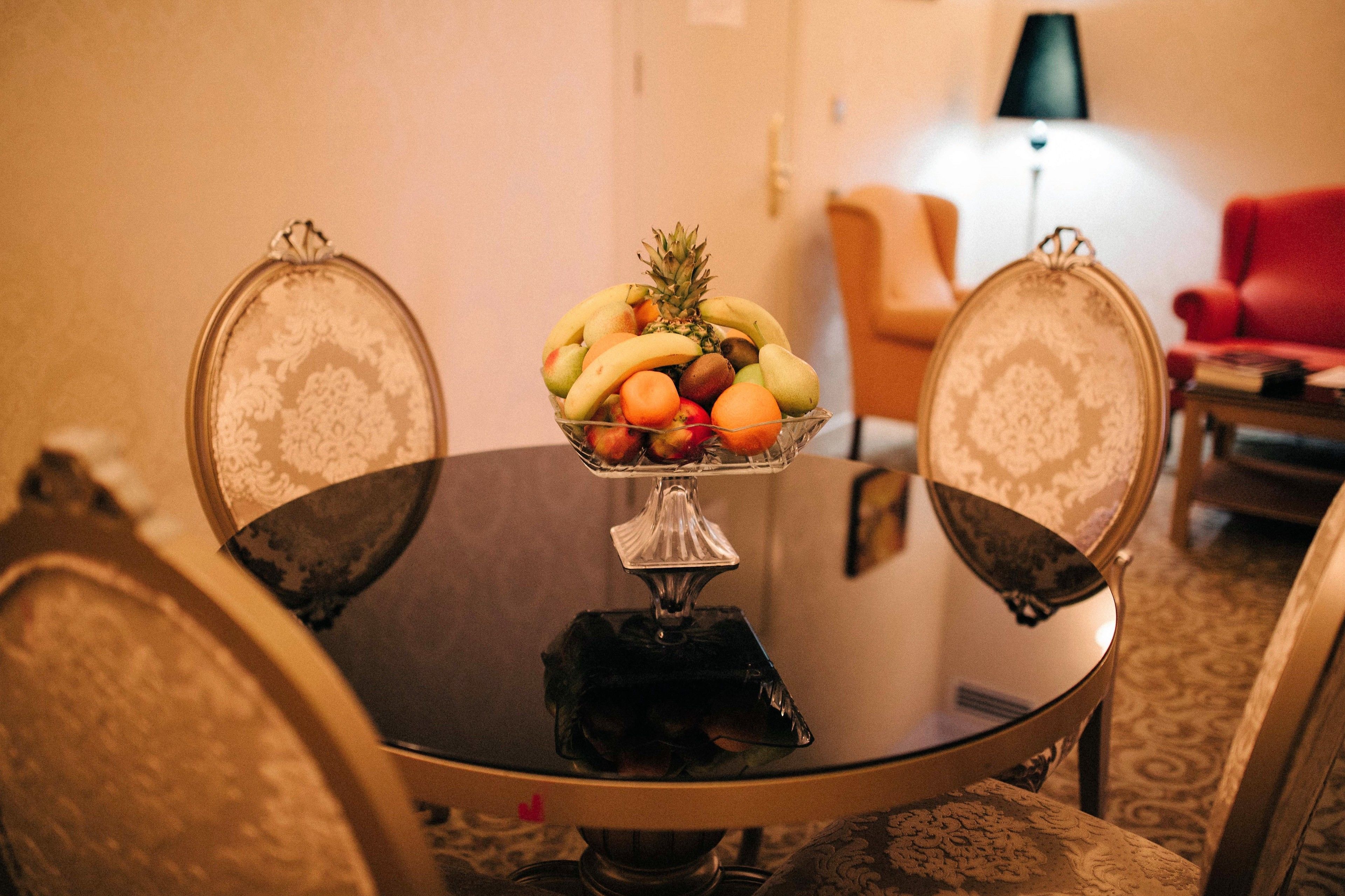 Une table à manger avec un saladier de fruits au centre, entourée de chaises rembourrées ornées d’un motif floral.