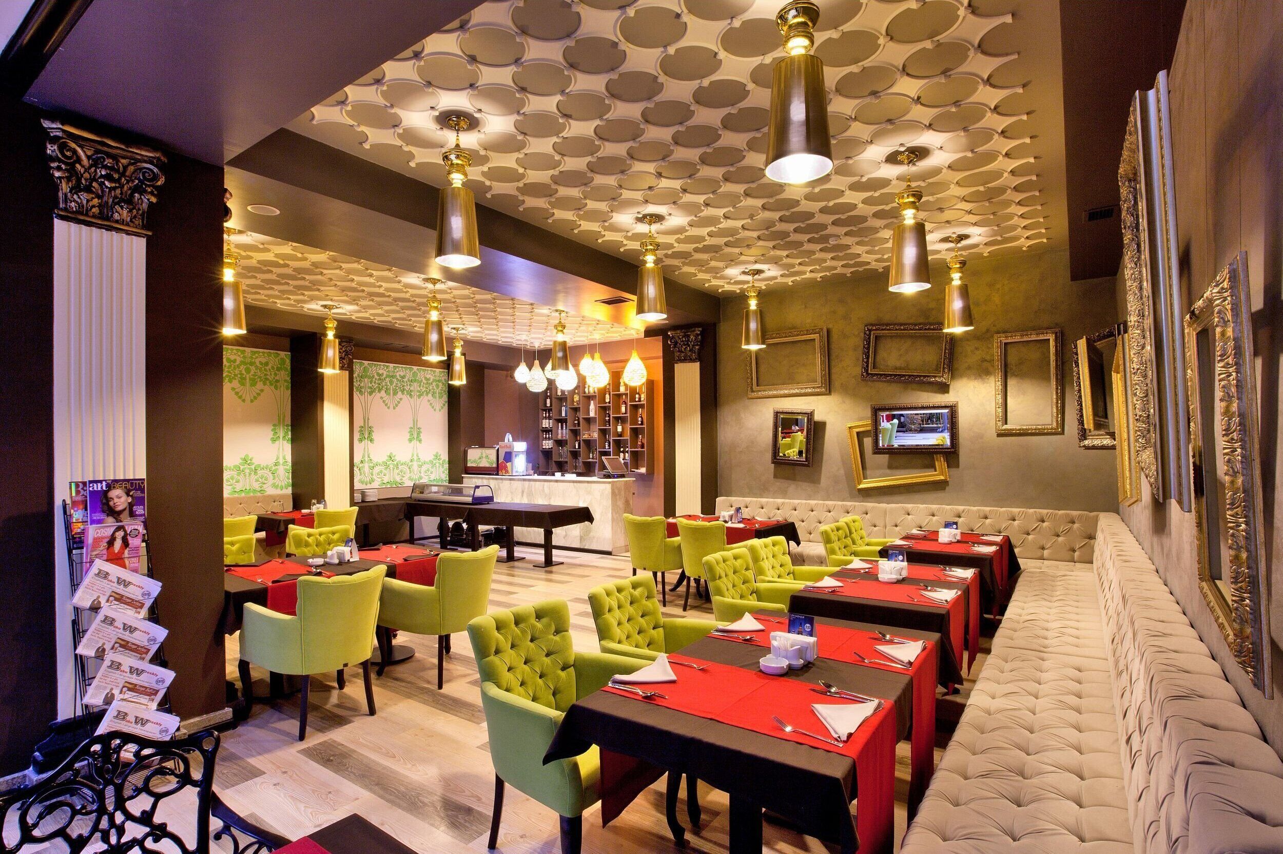 Un restaurante con techo estampado, sillas tapizadas de verde y manteles rojos.