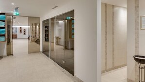 A hotel corridor with glass doors leading to rooms, a tiled floor, and a small table with a bowl on the right. - Hotel Albona Nova (Lech am Arlberg)