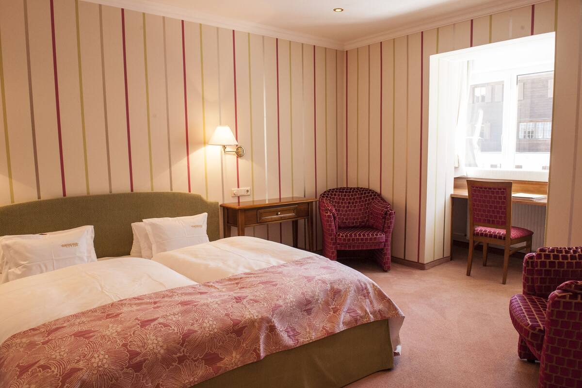 A hotel room with a bed, two chairs, a desk, and a window.