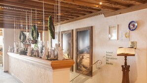 A reception area with a wooden counter, hanging decorations, framed pictures on the wall, and a lamp on a stand. - Hotel Albona Nova (Lech am Arlberg)