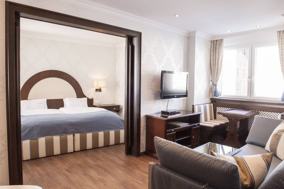 A hotel room with a large bed, a desk with a television, and a seating area with a view of the city.