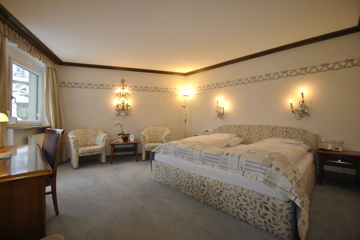 A bedroom with a large bed, two chairs, a desk, and a nightstand.