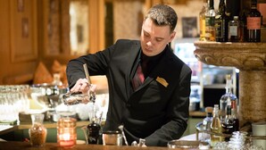 A bartender pouring a drink at a bar with various bottles and glasses. - Hotel Albona Nova (Lech am Arlberg)