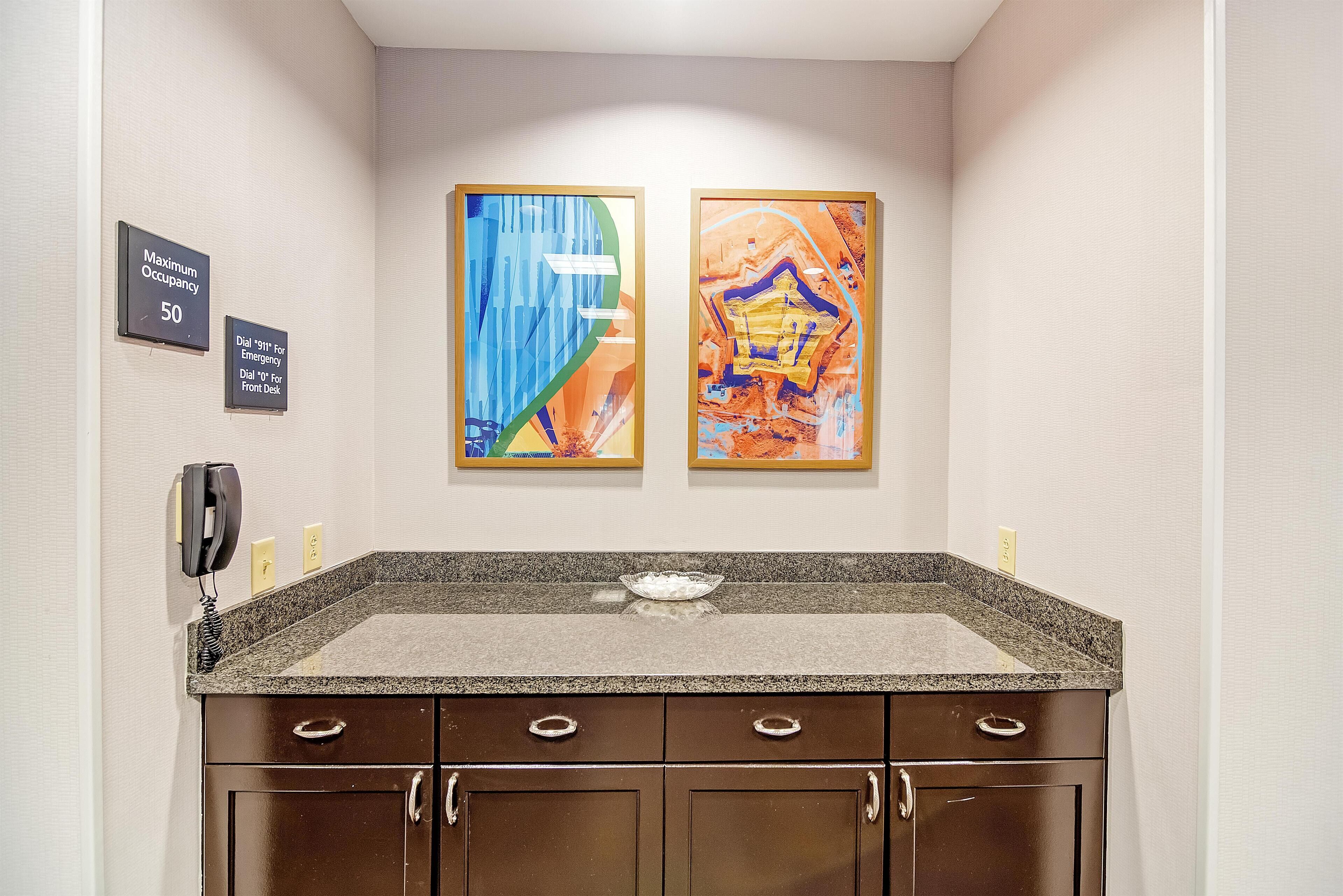 A bathroom with a granite countertop, a phone, and two framed artworks on the wall.