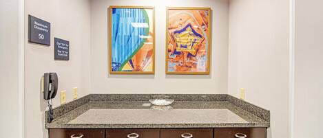 A bathroom with a granite countertop, a phone, and two framed artworks on the wall.