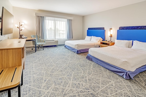 Une chambre d’hôtel avec deux lits, un bureau, une chaise, une télévision et une grande fenêtre avec des rideaux.