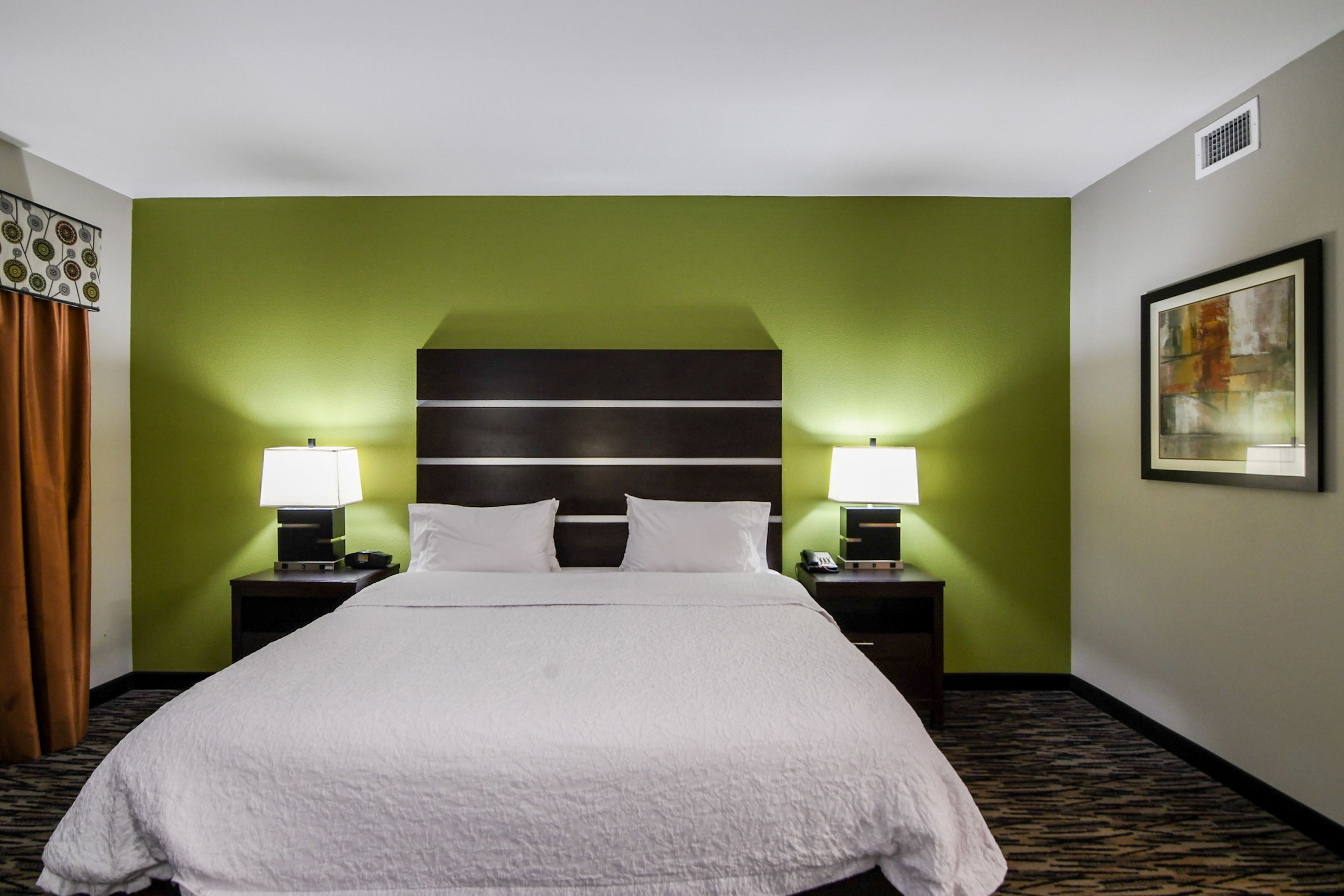A hotel room with a large bed, green walls, and a framed picture on the wall.